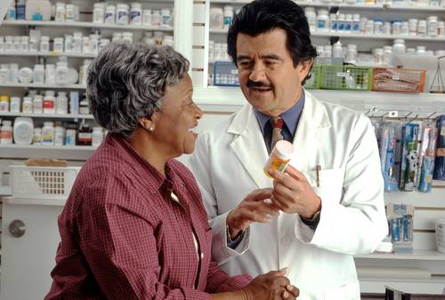 A Canadian pharmacy counter with prescription receipts and a patient discussing medication costs with a pharmacist
